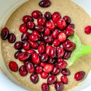 Adding cranberries in the batter for cranberry bread in a bowl.