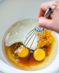 whisking eggs with milk, oil, and zest in a bowl.