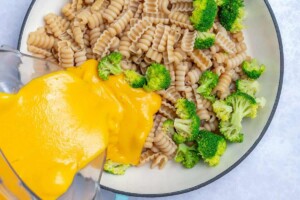 pouring the cheese sauce over pasta and broccoli in a pan.