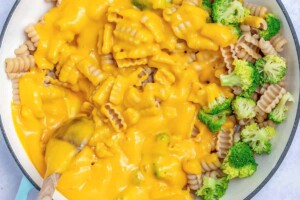 Mixing cheese sauce with pasta in a pan.