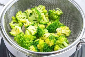 Steamed broccoli in a basket over a pot.