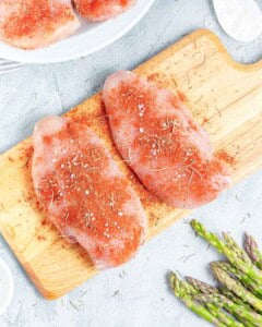 Chicken breasts seasoned with seasonings on a cutting board.