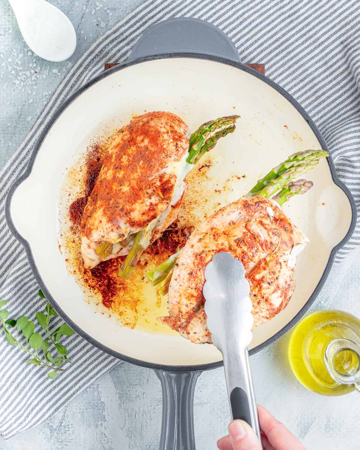 tongs grabbing cooked chicken breast stuffed, in a pan.