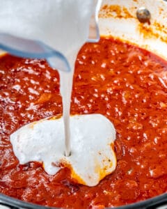 coconut cream sauce being added over the butter chicken sauce with in a pan