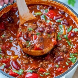 top view of a pot with beef chili with a wooden spoon full of chili and chili topped with fresh cilnatro