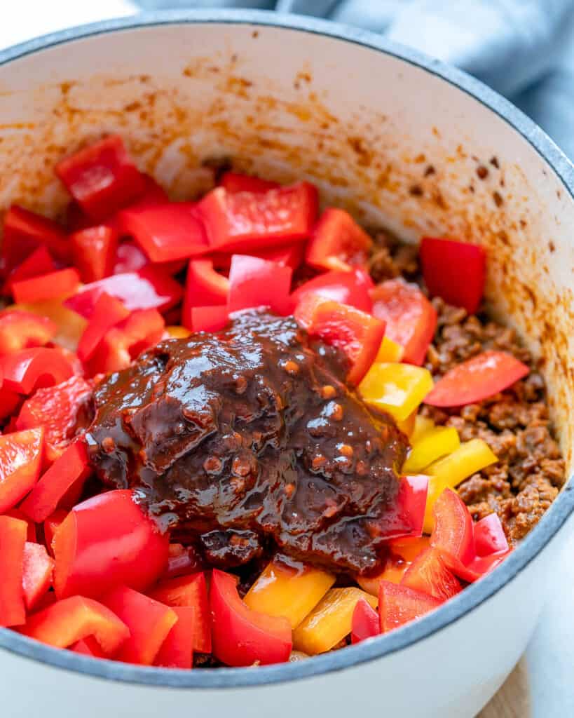 ancho chili paste with chopped peppers added over groud beef in a pot
