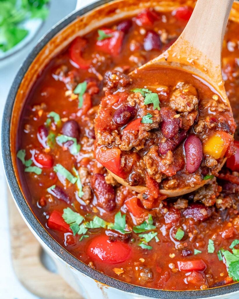 wooden spoonful of homemade beef and bean chili over a pot of chili
