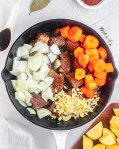 Carrots. Chopped onions and garlic are added over the beef in a skillet.