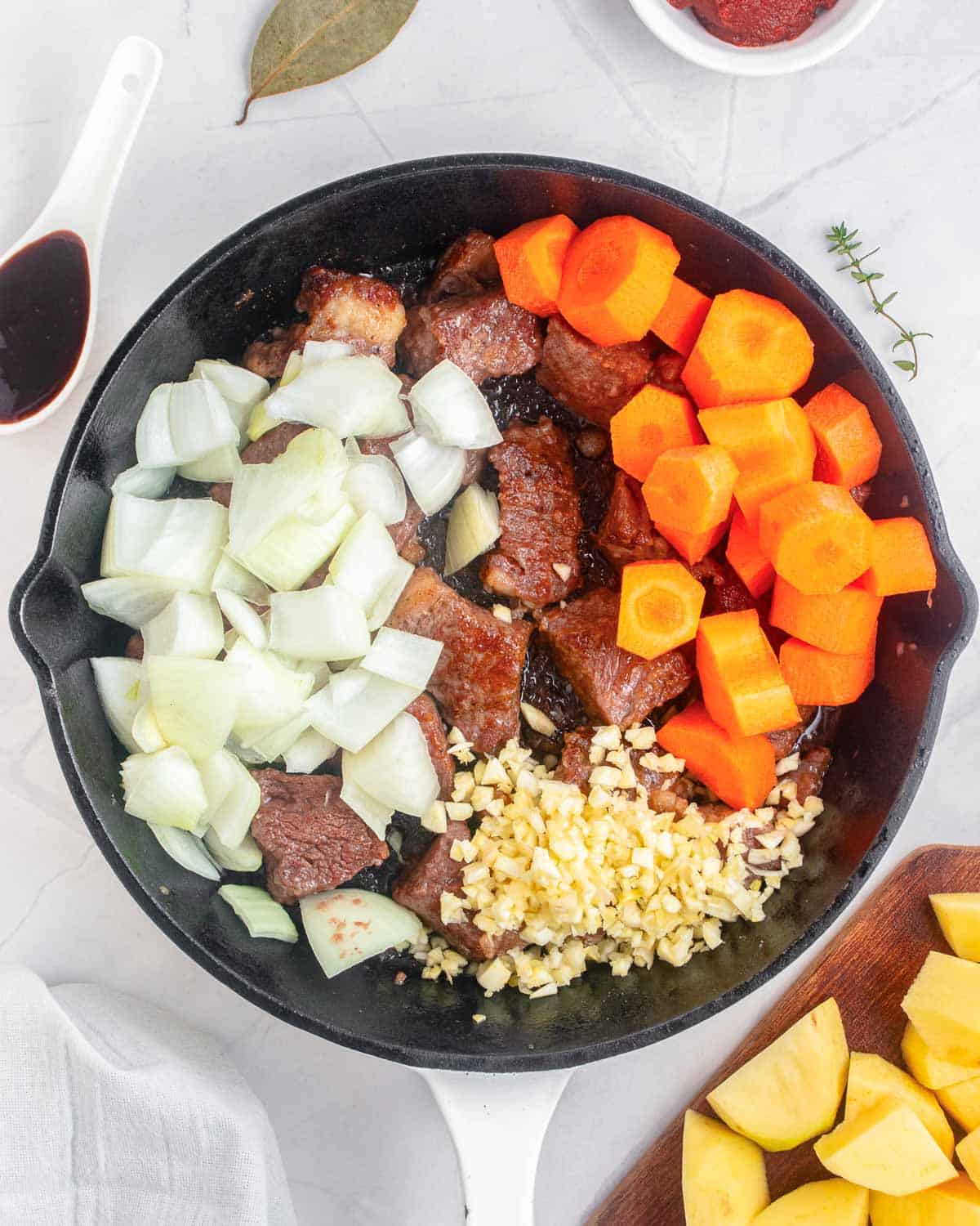 Carrots. Chopped potatoes, onions, and garlic are added over the beef in a skillet.