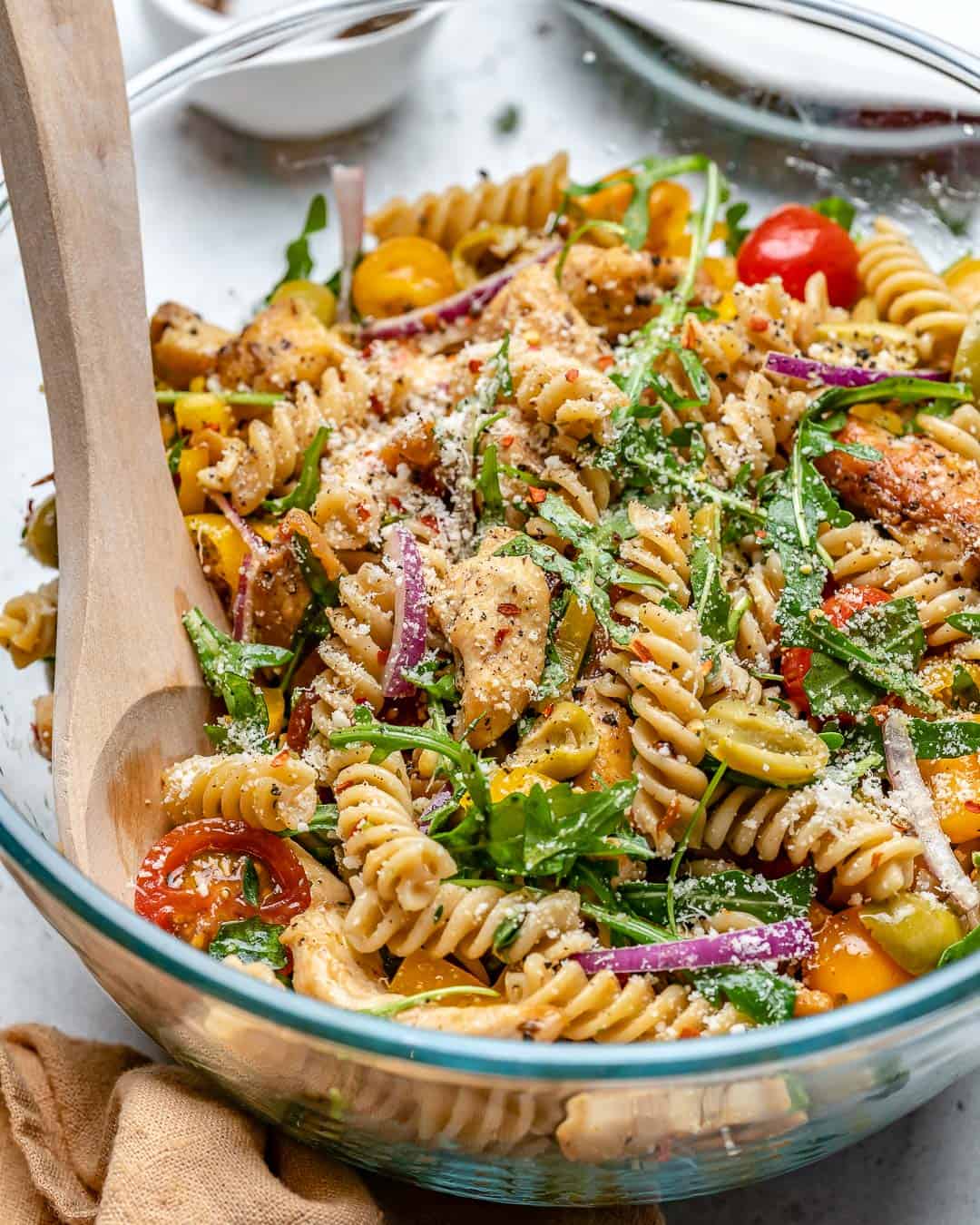 chicken pasta in a clear bowl with wooden spoon in it.