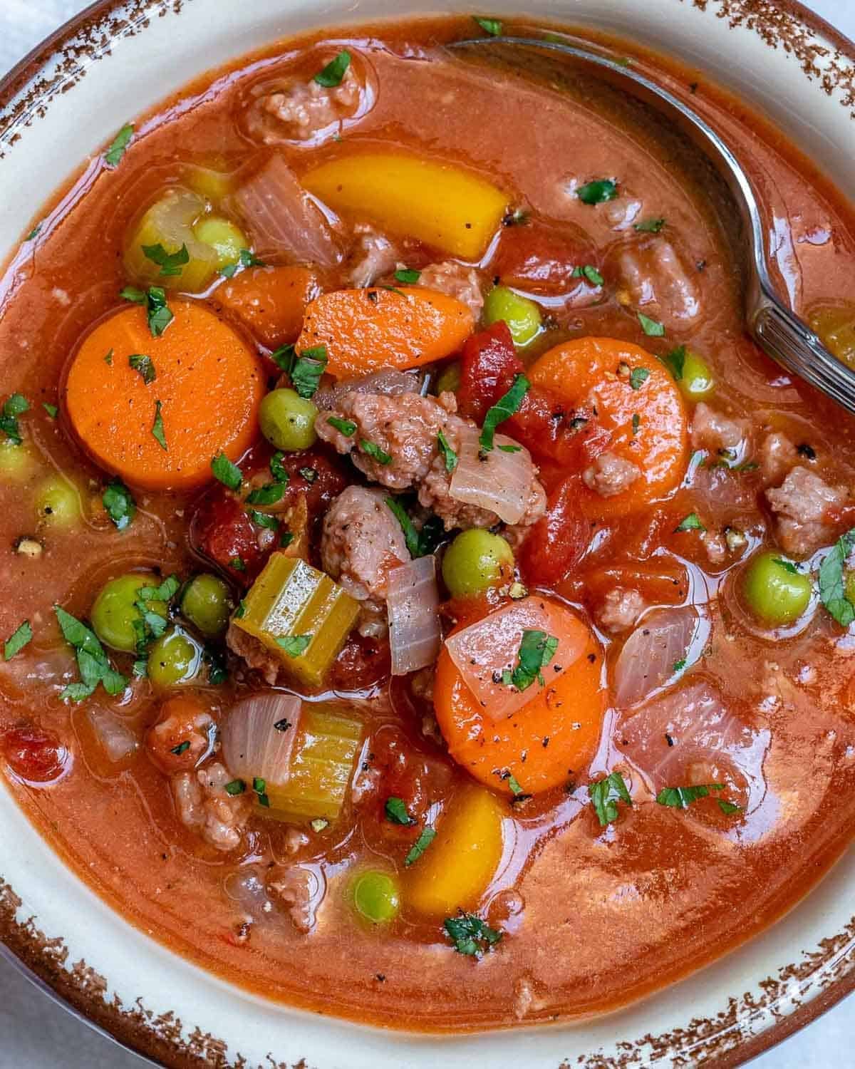 a bowl full of hamburger soup with sliced carrots and green beans.