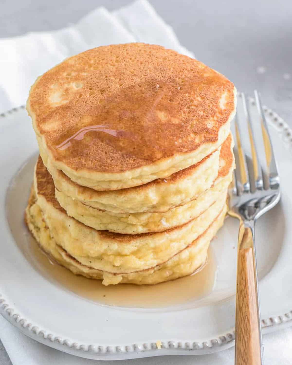 pancakes on a plate topped with syrup and a fork to the right.