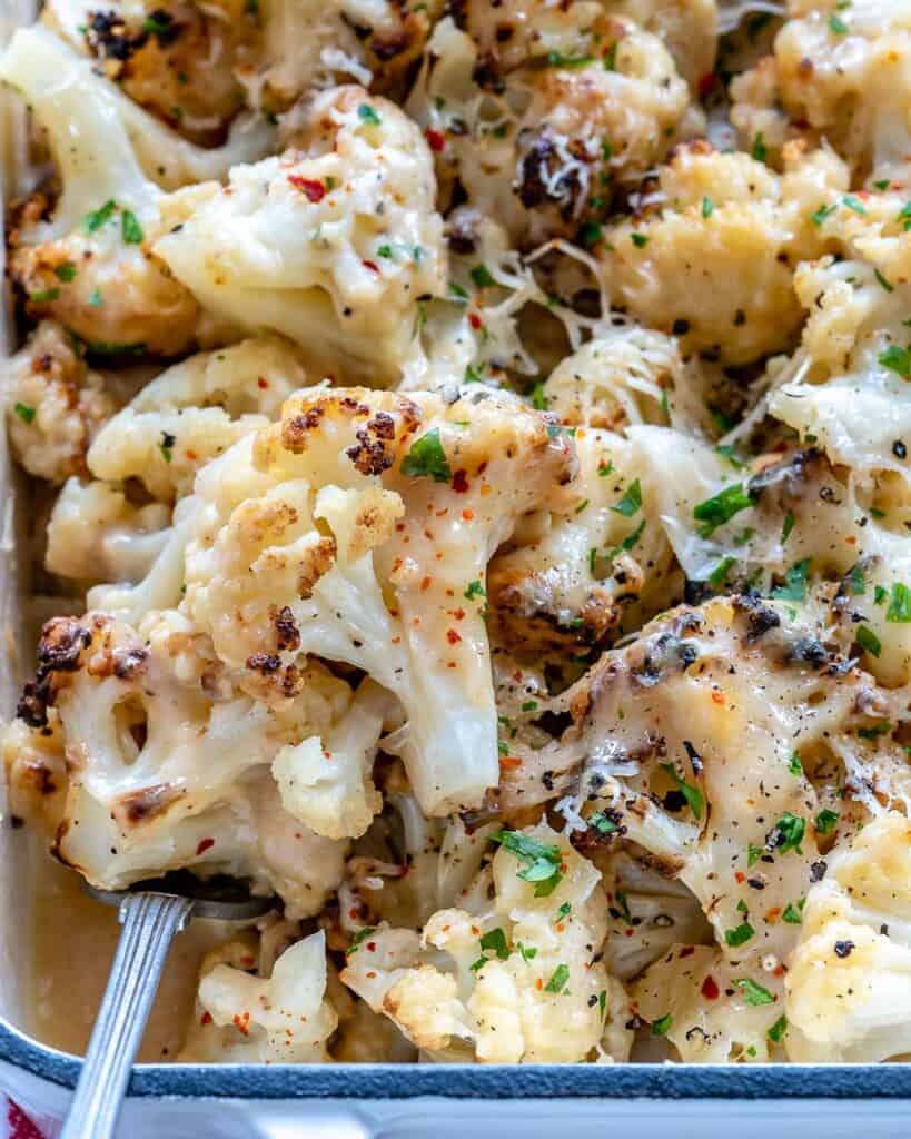 close up top view of a spoonful of baked cheesy cauliflower florets over a dish