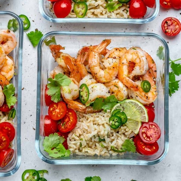 meal prep bowl with sauteed shrimp and a side of brown rice topped with chopped tomatoes and lime wedges.