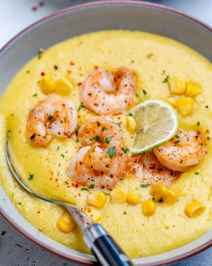 close up view of a bowl or yellow colored potato leek soup topped with sauteed shrimp with spoon in bowl