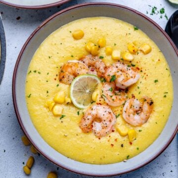 Top view of a round bowl with a yellow color potato and corn soup topped with sauteed shrimps