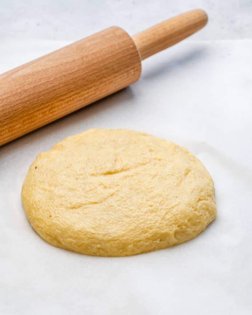 fathead  low carb pizza dough on a parchment paper next to a rolling pin 