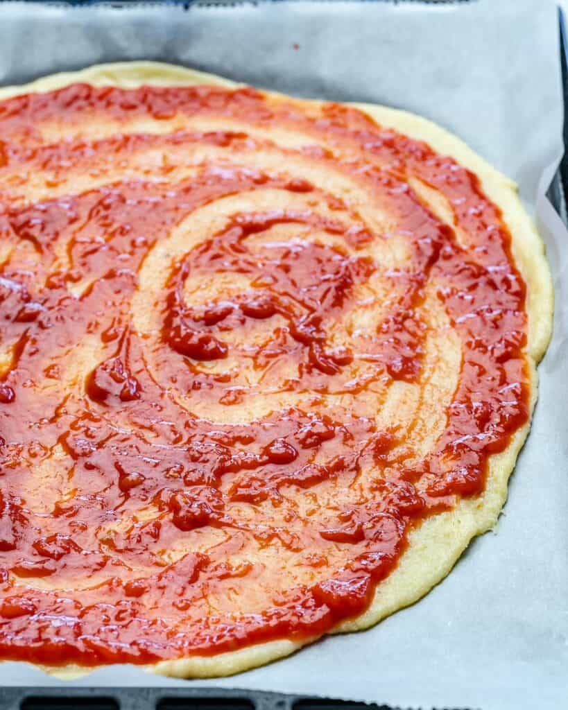 tomato sauce spread over thin pizza dough before baking 