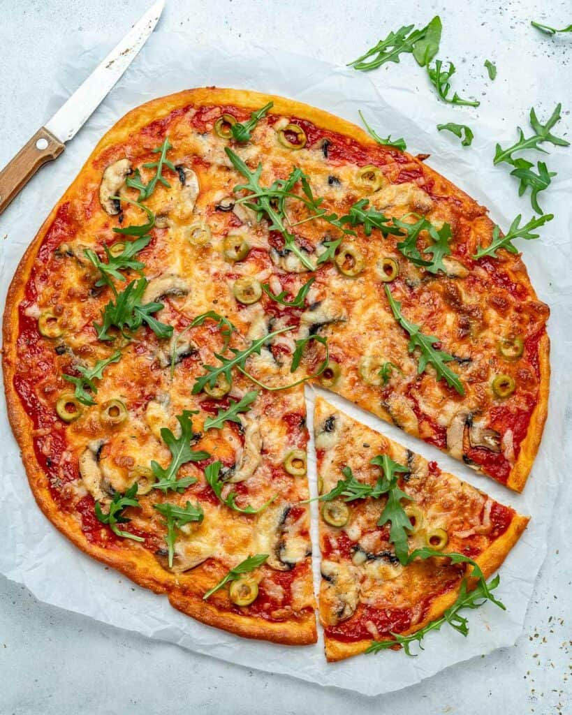 top view of a round pizza on a parchment paper with one slice cut out  