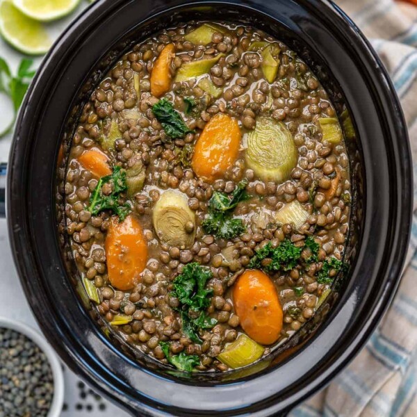 cooked lentil soup in a slow cooker with kale and chopped carrots.