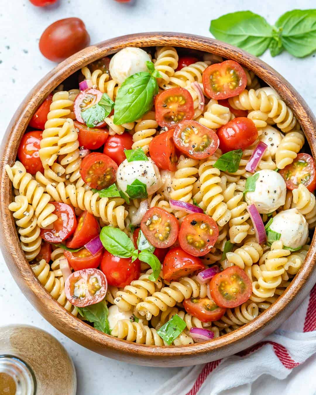 Caprese pasta salad in a round wooden bowl.