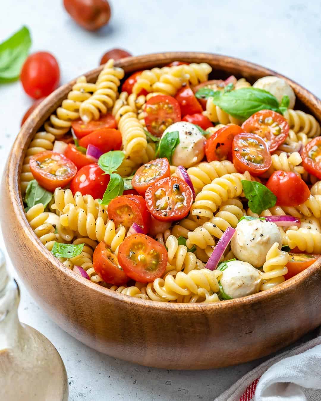 pasta salad recipe with cheese balls, fresh basil, and tomatoes.