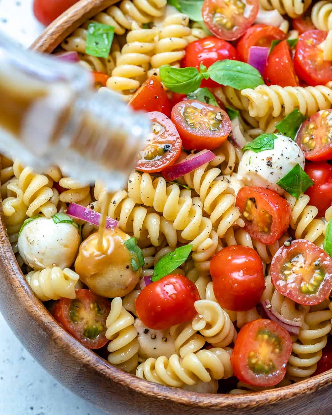 dressing being poured over a pasta salad bowl.