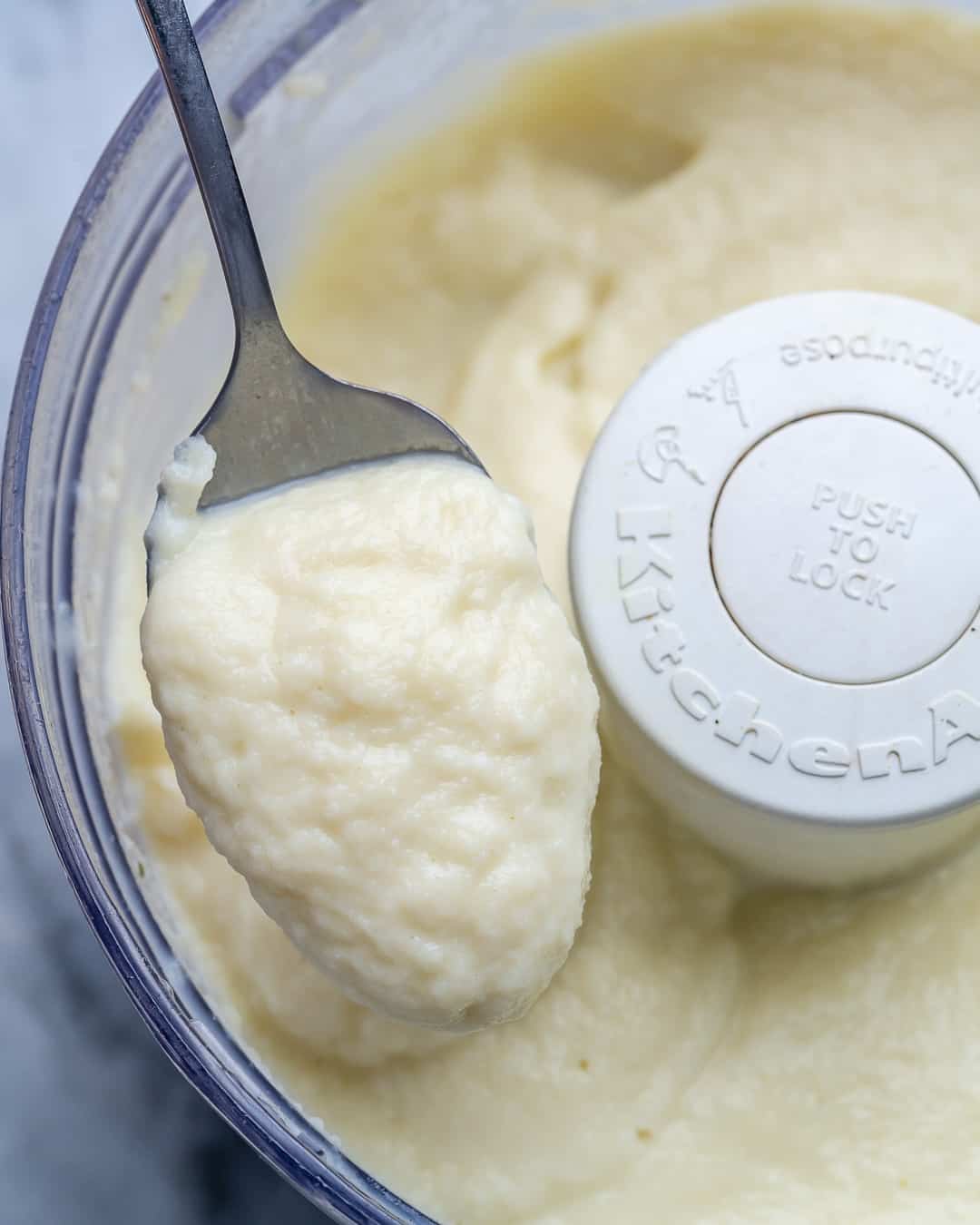 blended cauliflower sauce in food processor with a spoonful of the sauce