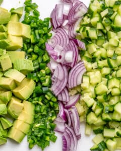 avocado, cilantro, onion, cucumber, chopped on a cutting board.