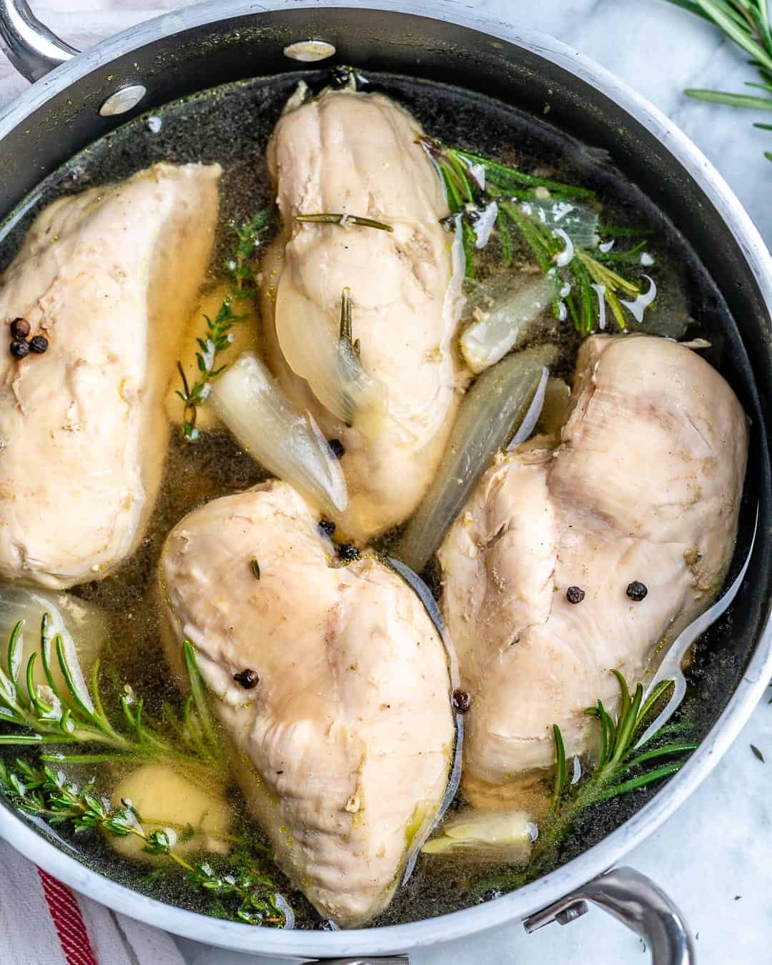 Poached chicken in pot with broth and herbs