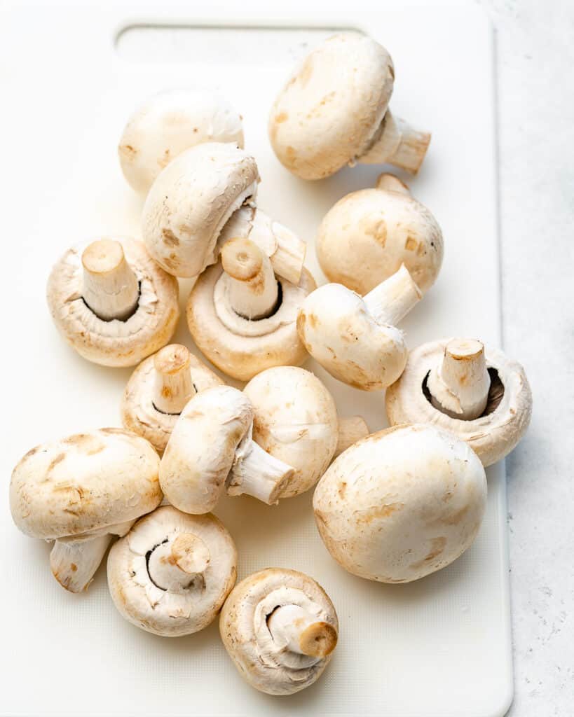 fresh white whole  mushrooms on a white cutting board