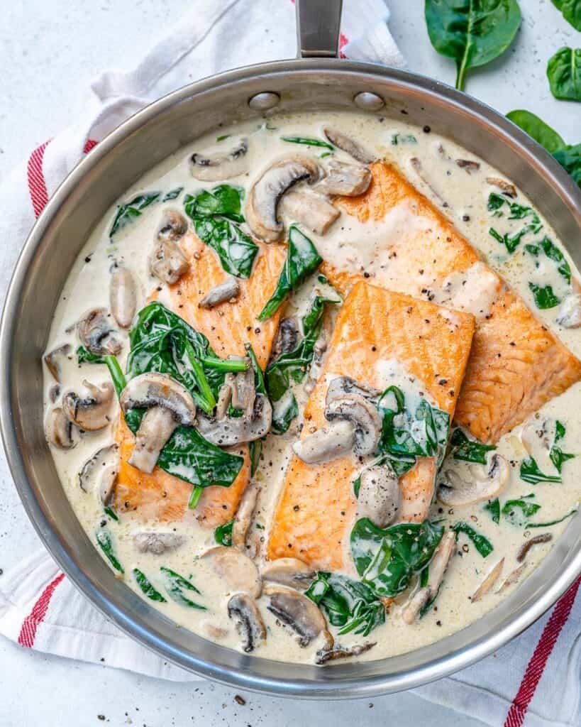 top view of a silver skillet with 3 salmon filets in a creamy white mushroom and spinach sauce
