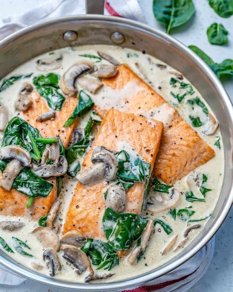 side view of 3 cooked salmon filets in a creamy mushroom and spinach sauce 