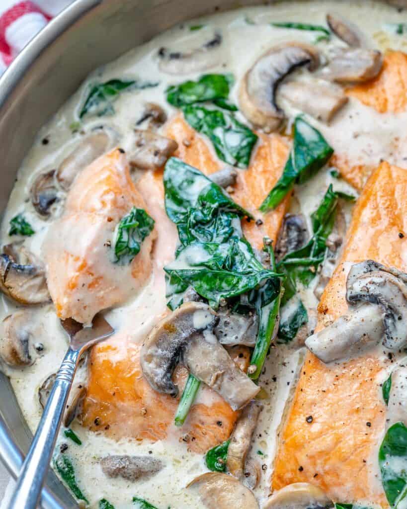 spoon in a pan with a cooked salmon filets in a creamy mushroom and spinach sauce