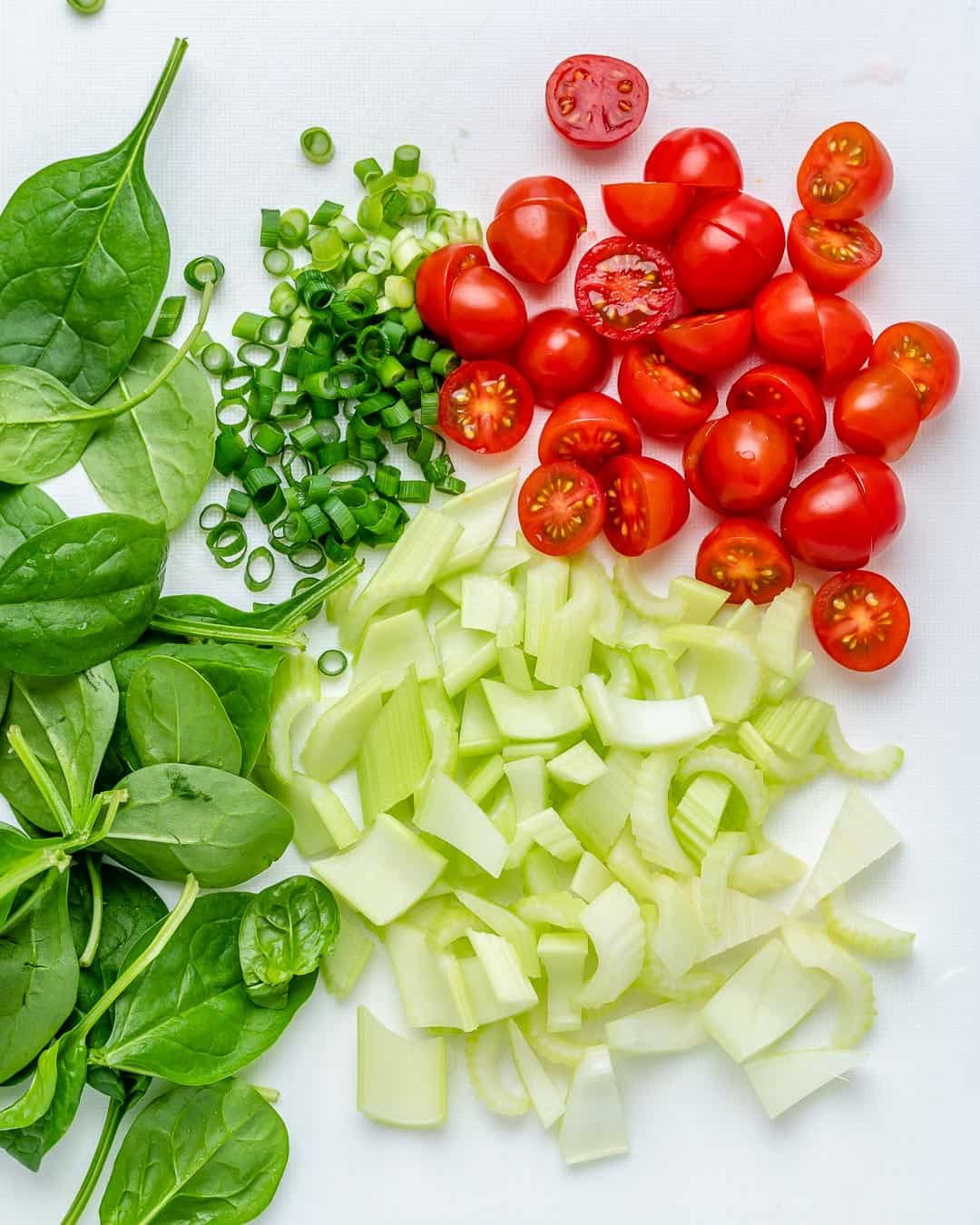 chopped cherry tomatoes, chopped celery, chopped onions, and chopped spinach on a cutting board