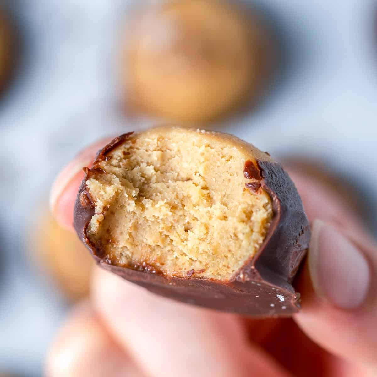 hand holding a peanut butter ball with a bite taken off it.