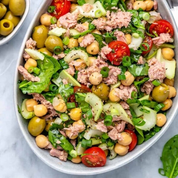 an oval white bowl with Chickpea tuna salad that has veggies like chopped tomatoes, celery, onions, and olives.