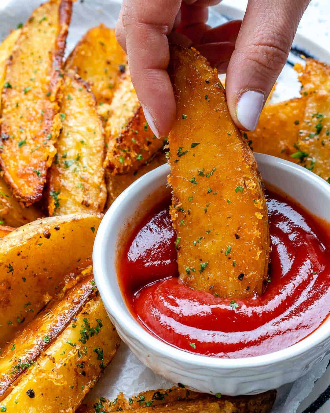 hand holding potato wedges and dipping in ketchup