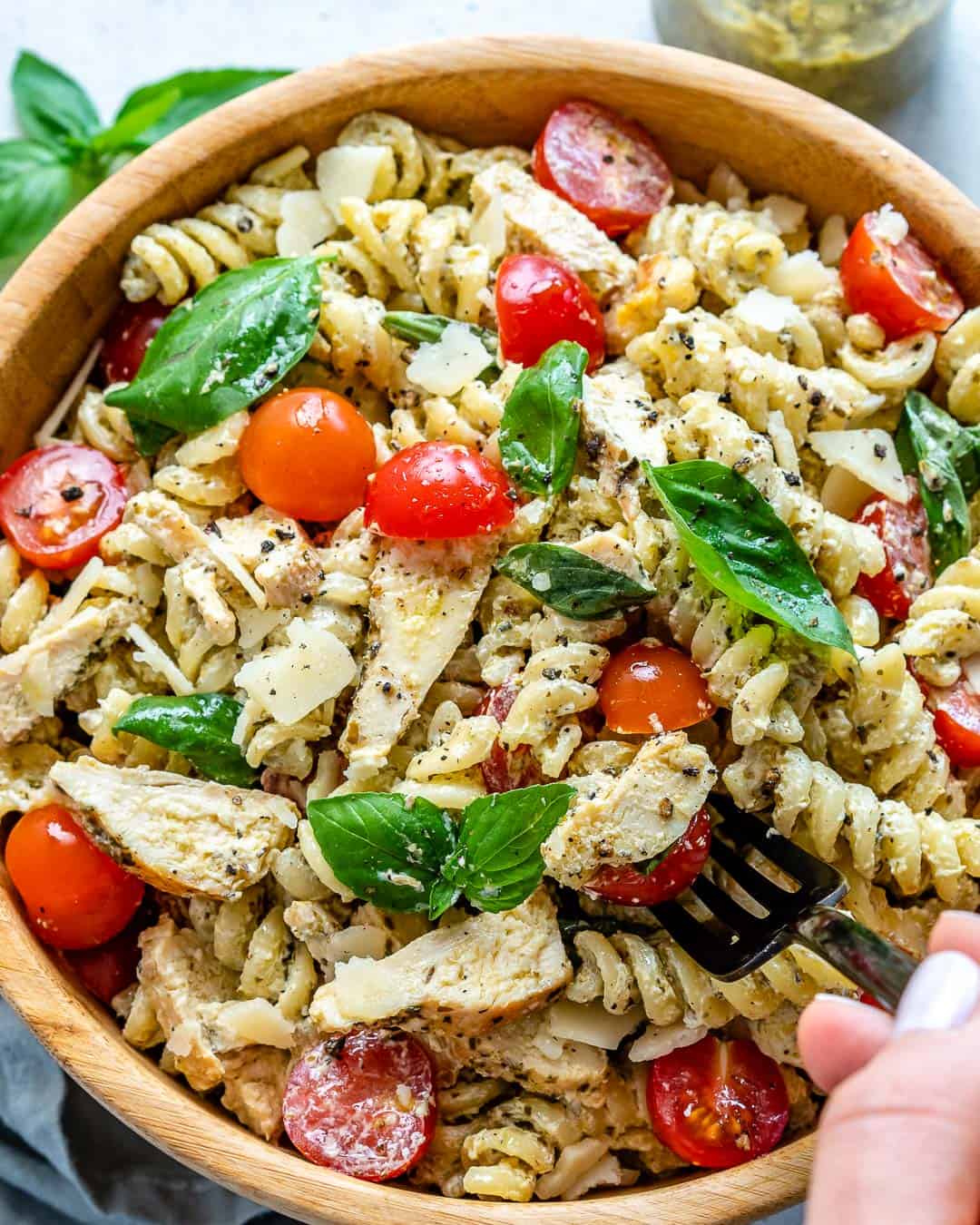 hand holding fork reaching for some pesto pasta in a bowl.