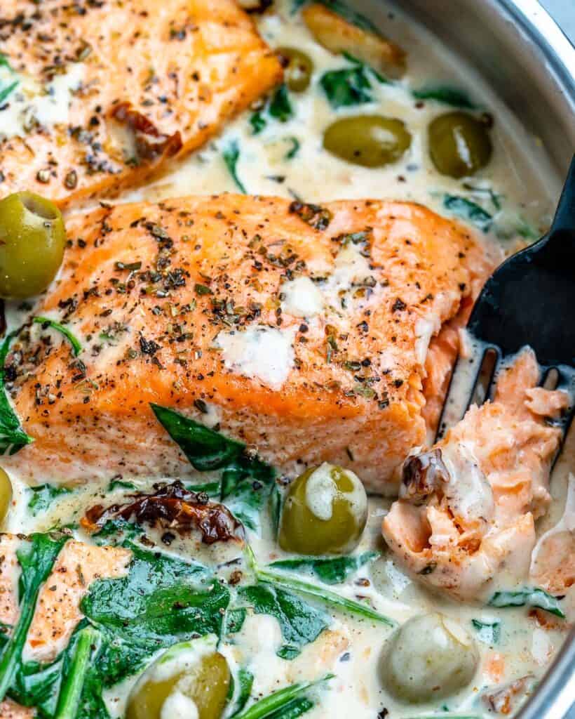 fork in salmon flaking it in a creamy sauce in a pan