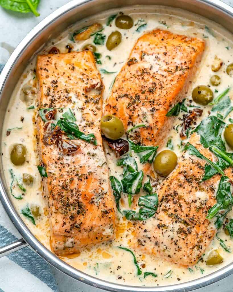 overhead shot of  cooked salmon filets in a creamy Tuscan sauce with olived