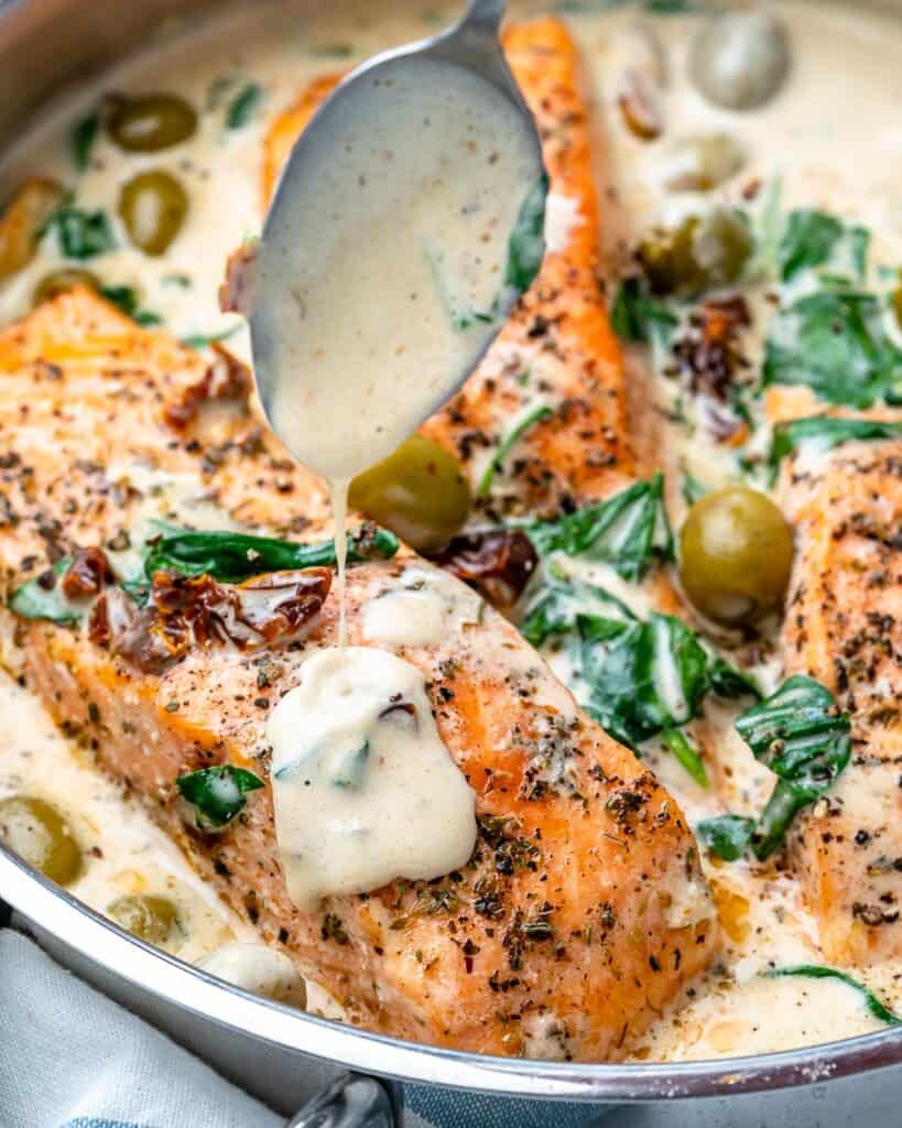 creamy sauce drizzling over salmon fillet in a skillet