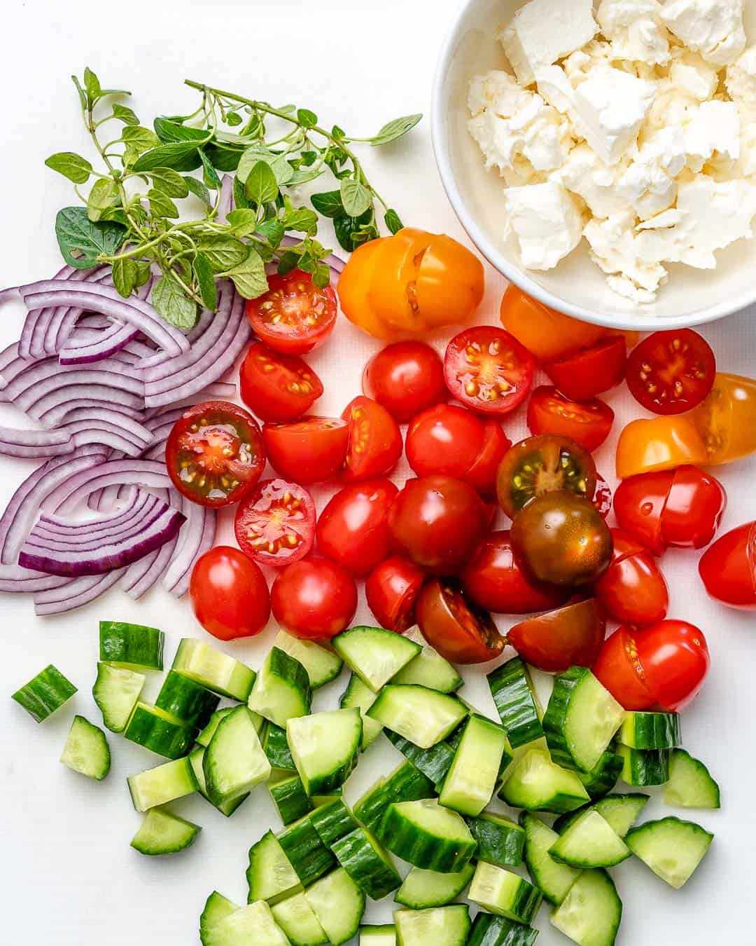 veggies for the salad cut up on a cutting board with a side of feta cheese