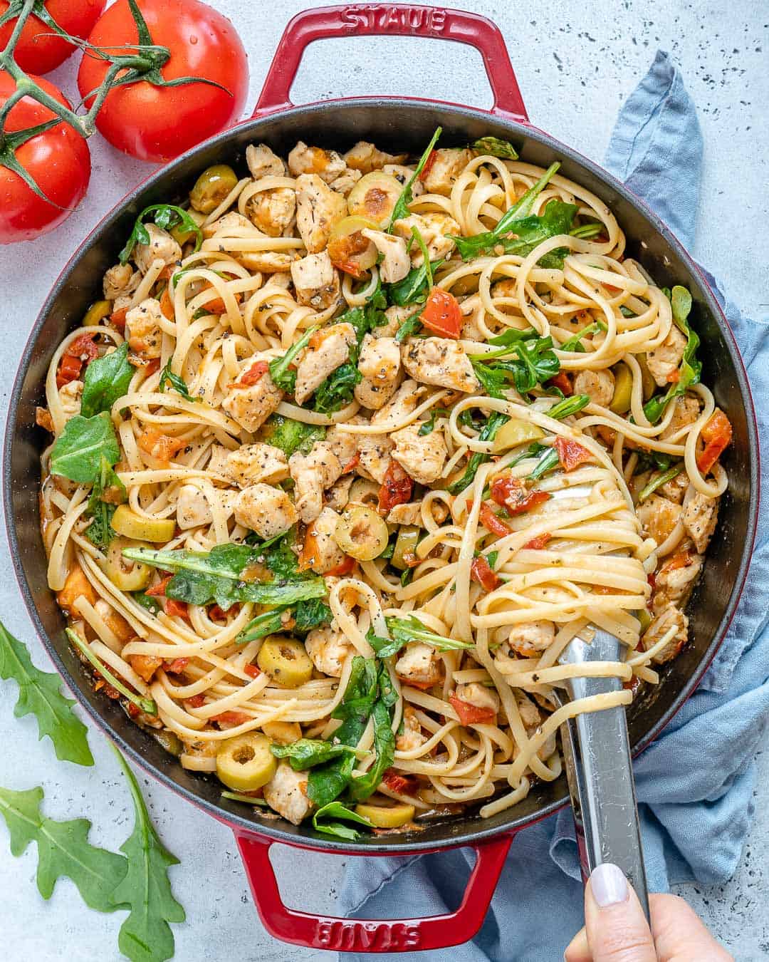 chicken spaghetti in a red skillet which utensil grabbing some pasta. 