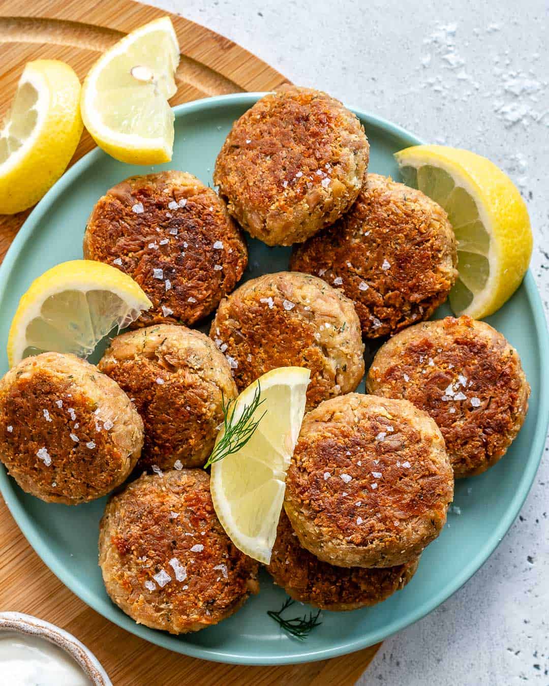 tuna cakes on a blue plate with lemon wedges as garnishes