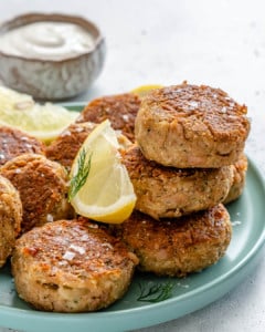 patties made with tuna stacked on a plate with lemon wedged and a side of dip