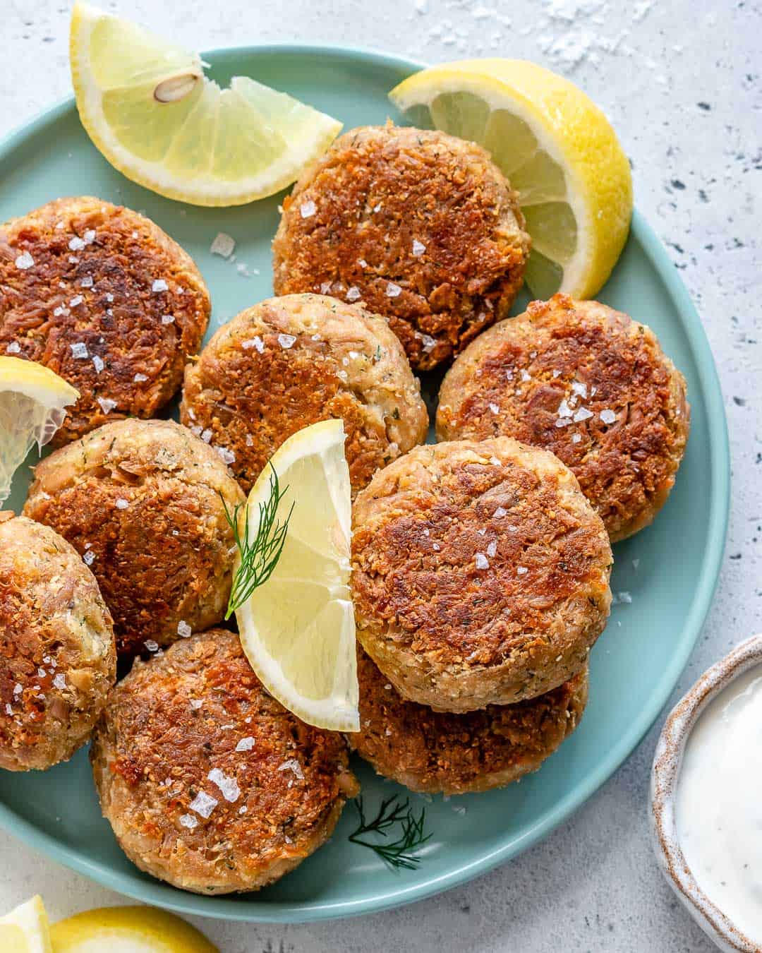 tuna patties on a plate with dill and lemon wedges garnishes