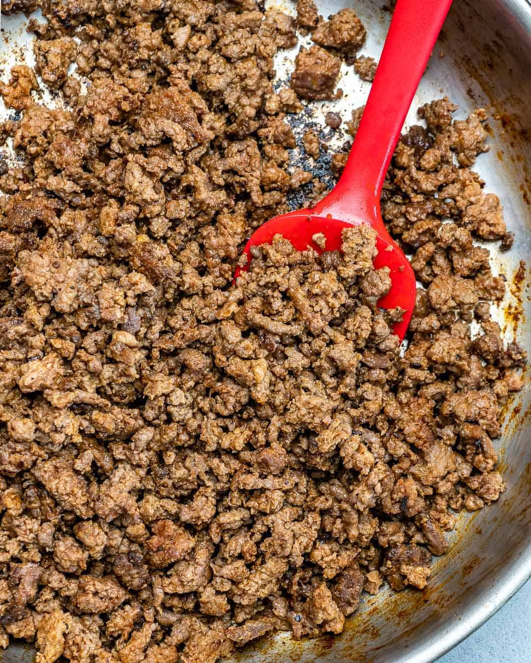 cooked ground beef in skillet with red spatula in it 