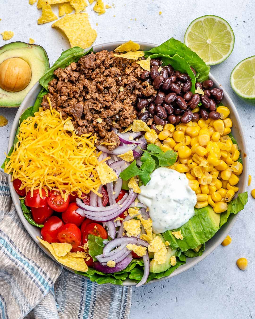 top view taco salad in a bowl and garnishes on side of bowl