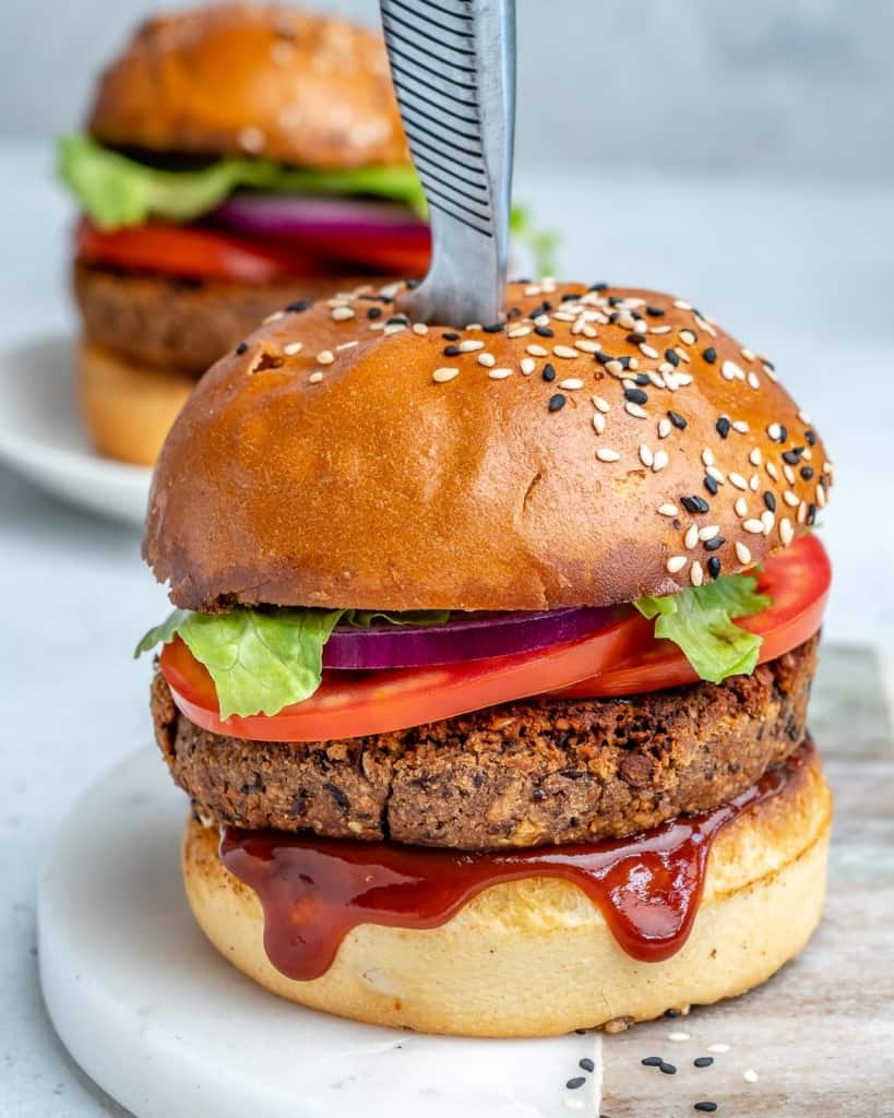 knife in the middle of a black bean burger with bbq sauce dripping out 